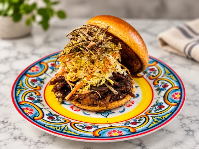 A sandwich with shredded filling and slaw on a colorful patterned plate.