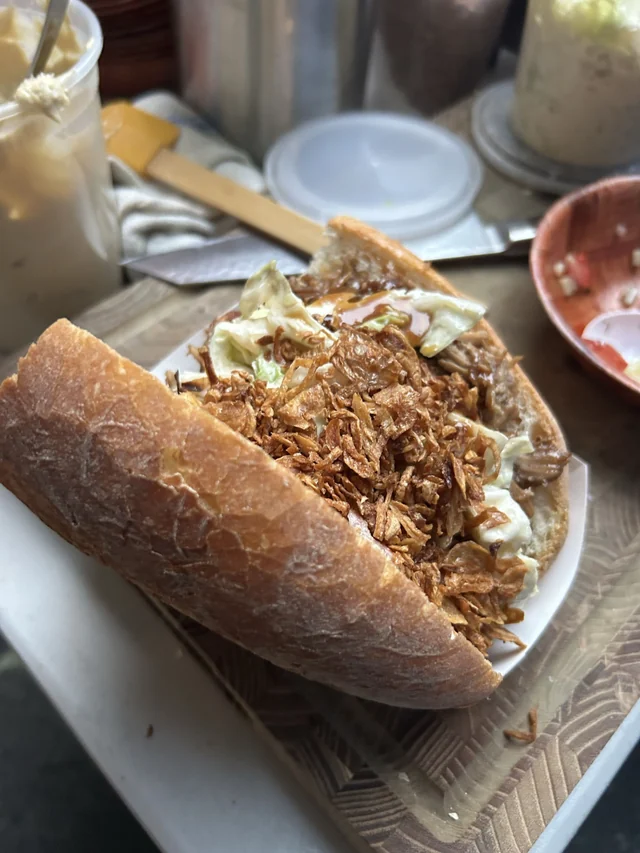 A close-up of a sandwich with shredded filling, slaw, and crisp toppings.
