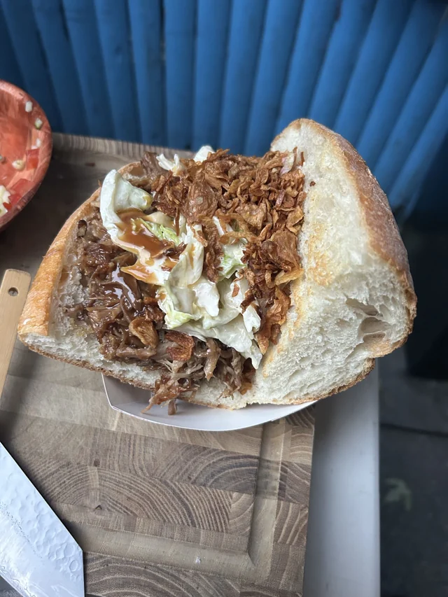 A filled sandwich with slaw and crisp toppings, seen from above on a wooden board.